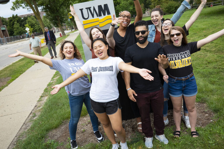 Students smiling in front of UWM sign.