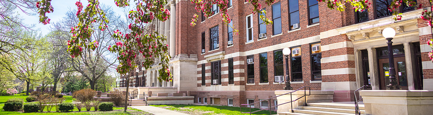 Mitchell Hall, A red brick university building surrounded by blooming spring trees and green lawns on a sunny day.