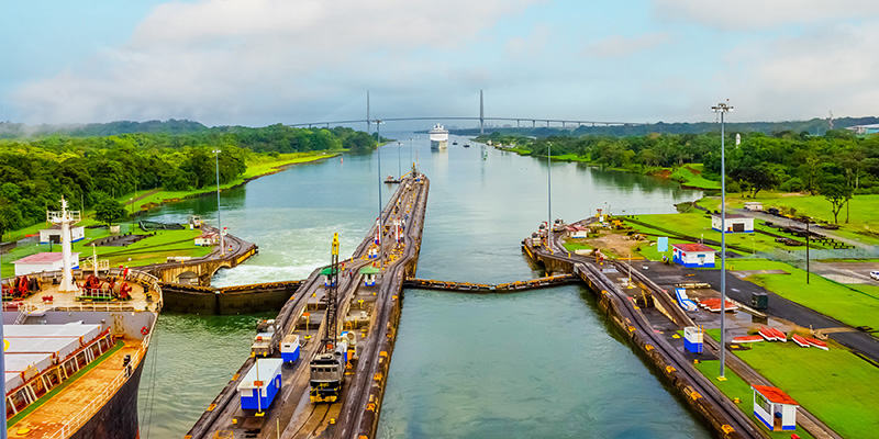 Panama Canal with ships floating nearby and a bridge in the background.