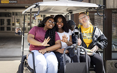 Three women pose for a picture sitting on a golf cart