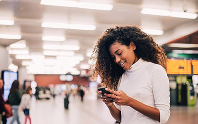 A woman is looking at her cell phone while she stands in a hallway