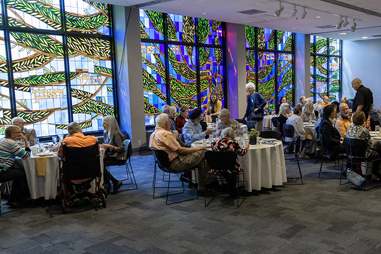 An across the room picture of the 2026 UWMRA luncheon with people sitting at tables and a large stained glass window is in the background.