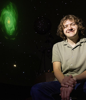 Nick Nelson sits in front of an image with stars and a dwarf novae.
