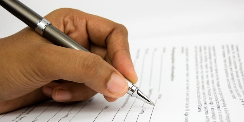 Close-up of a hand filling out a request form with a pen, emphasizing the process of submitting formal applications and documents.