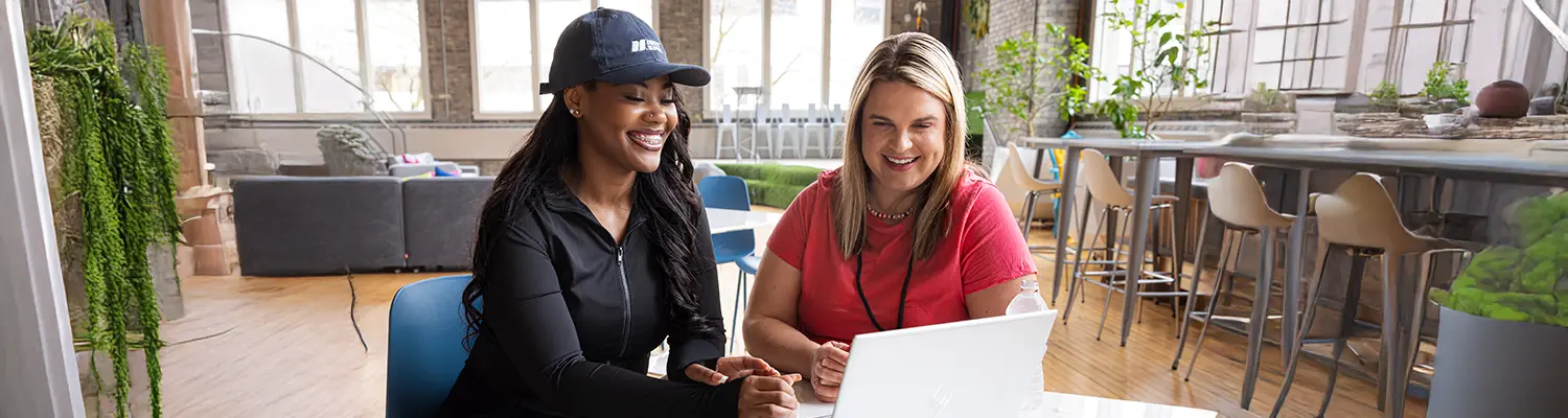 two people looking at a laptop on a table in an office environment