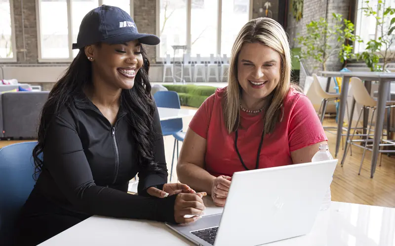 two people looking at a laptop on a table in an office environment