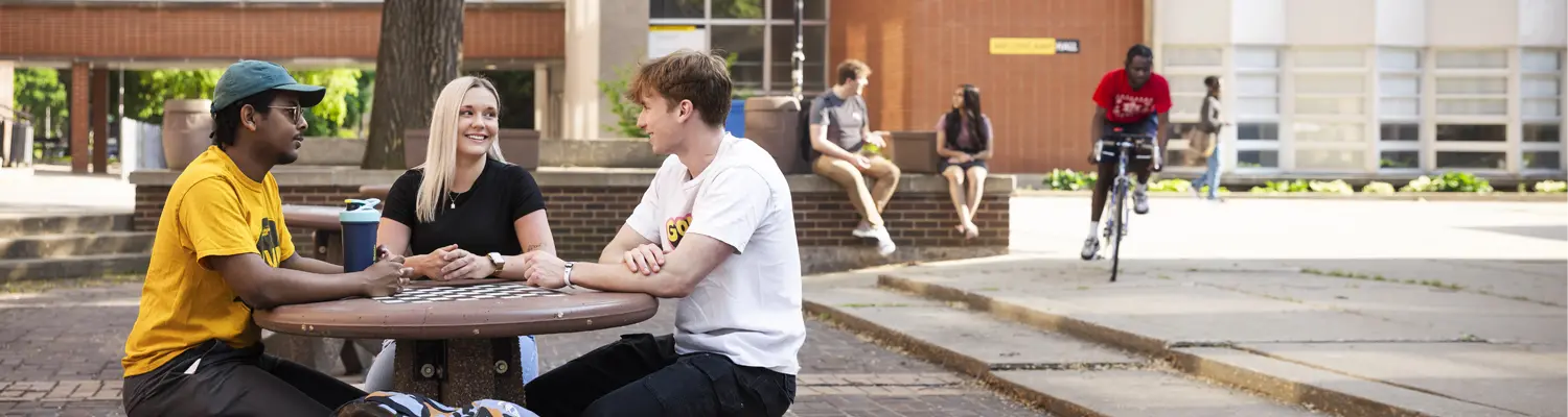 students sitting outside on UWM campus while another student bikes by