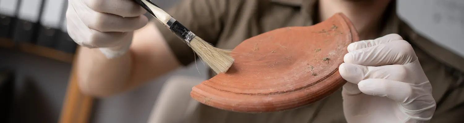 close up of hands using tools to clean pottery