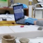 person using laptop while sitting next to museum pieces