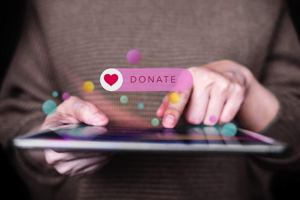 person holding tablet, index on the screen, with transparent Donate text and heart in middle of image.