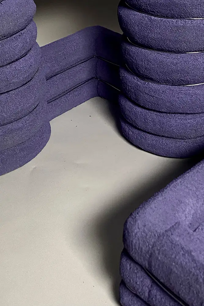 Close-up of a purple foam architectural model with stacked rounded forms connected by a narrow bridge, shown on a smooth light surface.