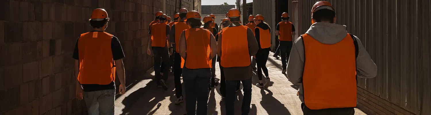 Students in hard hats and construction vests tour a site.