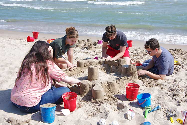 Architecture students build sand castles at the beach as part of their educational and social gatherings.