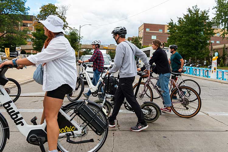 Urban Planning students walk their bikes across a street on campus during a welcome back ride and picnic.