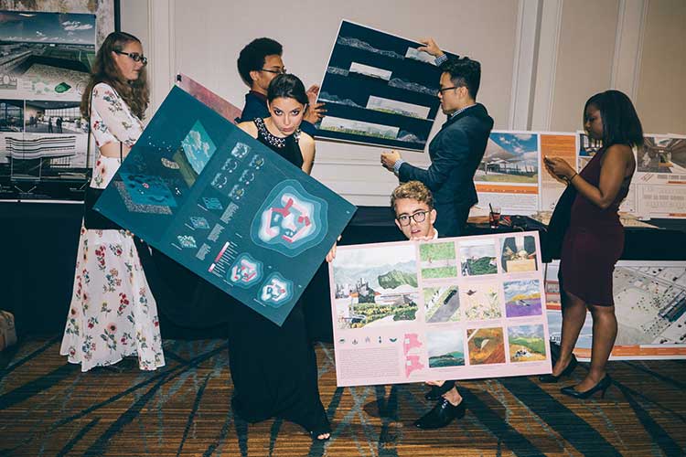 Architecture students in formal attire pose for the camera holding posters of their work at a social event.