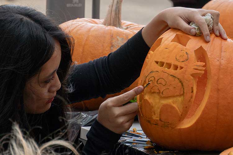 A student carefully carves a design onto a pumpkin at a social event.