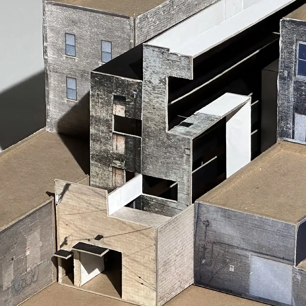 Close-up of an architectural model depicting an urban infill building with layered concrete façades, recessed openings, and a narrow passage between structures.
