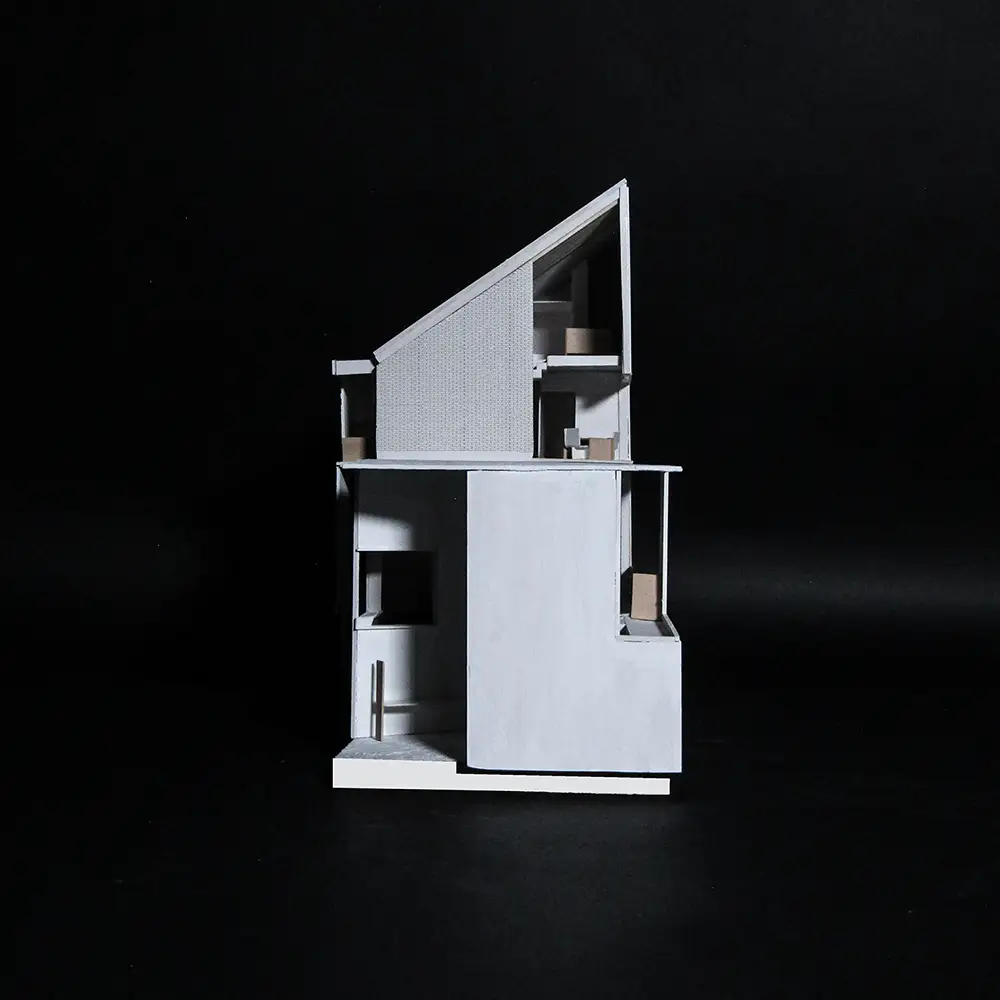 Cutaway architectural model of a compact house with a sharply sloped roof, showing interior rooms, balconies, and layered volumes against a black background.