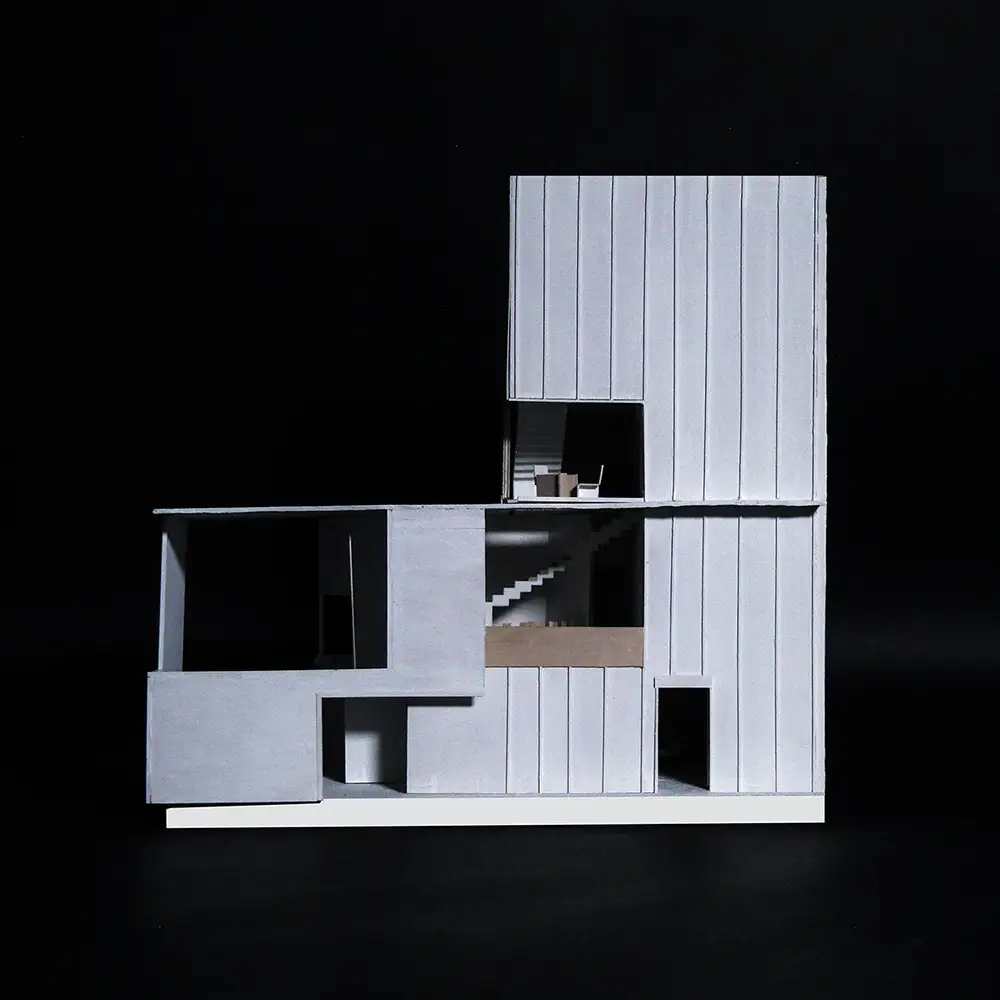 Section model of a modern house with vertical metal siding, revealing stairs, interior rooms, and layered volumes cut open against a black background.