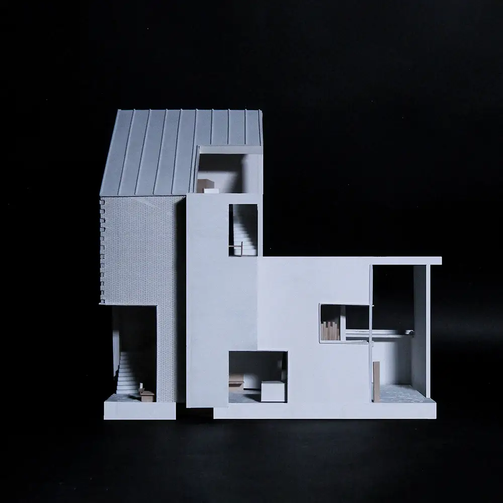 Section model of a modern house with a sloped metal roof, brick and smooth façades, and cutaway rooms showing stairs, seating, and living spaces.