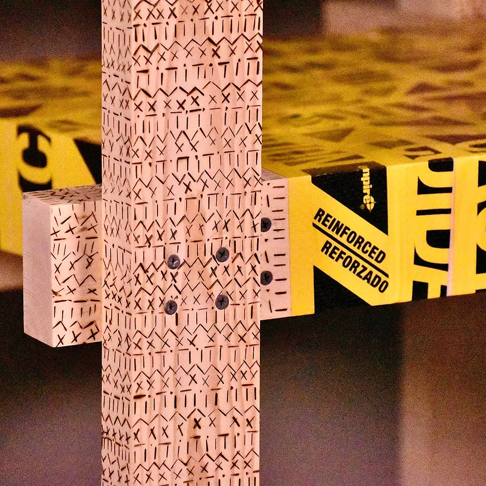 Close-up of a chair joint showing layered plywood components, visible screws, and yellow tape wrapped around the seat edge.