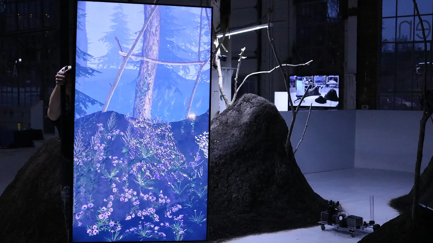 Digital screen showing a forest scene beside soil mounds and bare branches in an art installation.