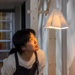 Iris Ma peers into a delicate paper-like lamp that hangs in the gallery.