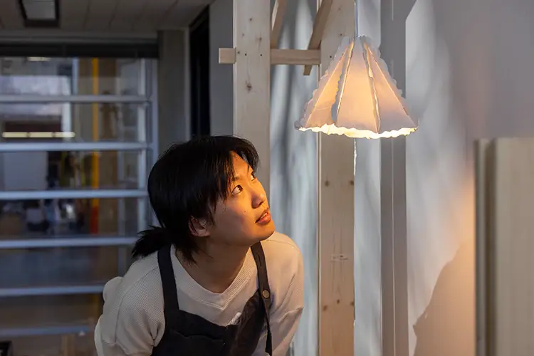 Iris Ma peers into a delicate paper-like lamp that hangs in the gallery.