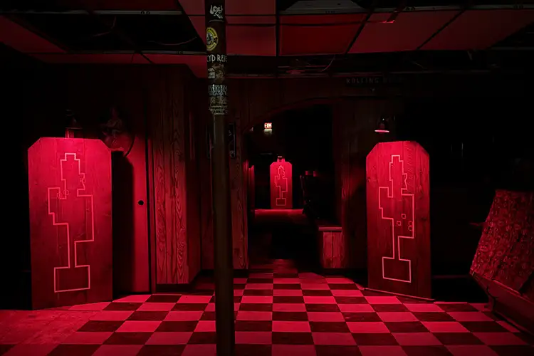 Red-lit “tombstone” tables marking architectural ghosts in a dark interior