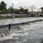 Flood waters rise nearly above a fence line in a commercial district.