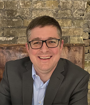 Headshot of Kyle Gast in front of a stone wall.