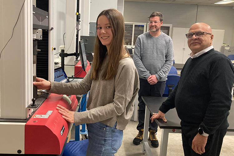 A student operates a lab equipment while two faculty members observe in a workspace.