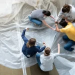 A view from above, students kneel while spreading large sheet of translucent material