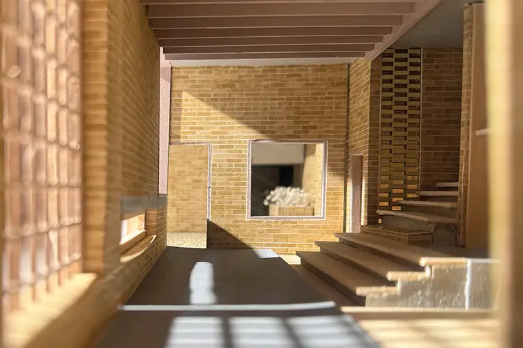 Sunlit architectural model interior with brick walls, stairs, and window opening.