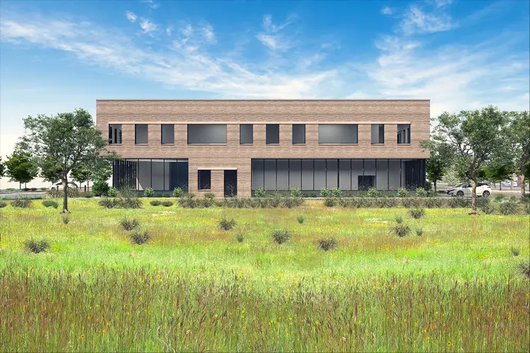 Two-story brick building with large windows set behind a grassy field with shrubs, under a blue sky with scattered clouds. Two-story brick building with large windows set behind a grassy field with shrubs, under a blue sky with scattered clouds.