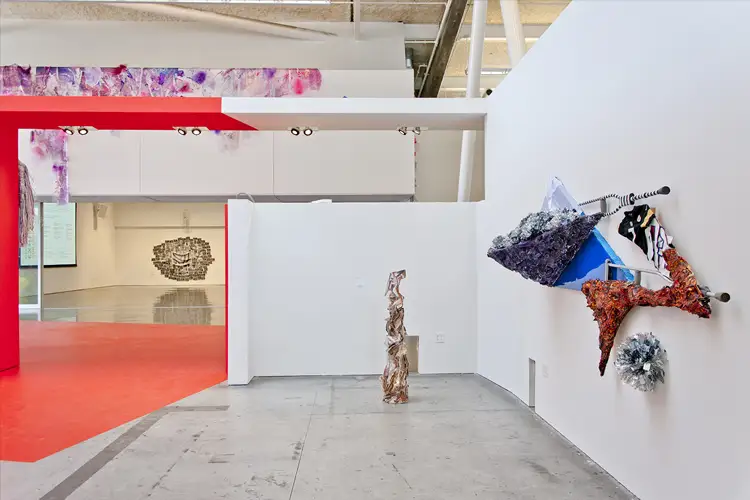 Contemporary gallery with white walls, red entry corridor, and sculptural artworks: a tall central column and colorful wall-mounted forms. Contemporary gallery with white walls, red entry corridor, and sculptural artworks: a tall central column and colorful wall-mounted forms.
