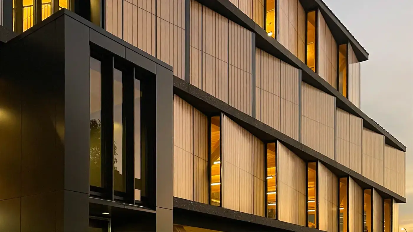 Modern multi-story building facade with vertical panels and glowing windows at dusk.