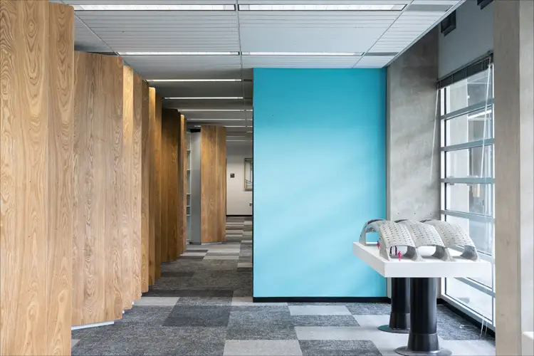 Hallway with wood panel columns, blue accent wall, carpet tiles, and a display table by windows with architectural models. Hallway with wood panel columns, blue accent wall, carpet tiles, and a display table by windows with architectural models.