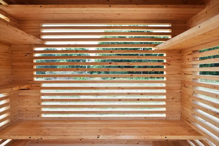 Interior view of a wooden slat structure with horizontal gaps, framing an outdoor scene with trees and landscape beyond. Interior view of a wooden slat structure with horizontal gaps, framing an outdoor scene with trees and landscape beyond.