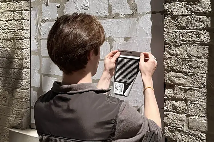 A student applies a vinyl sticker to a boarded up window.
