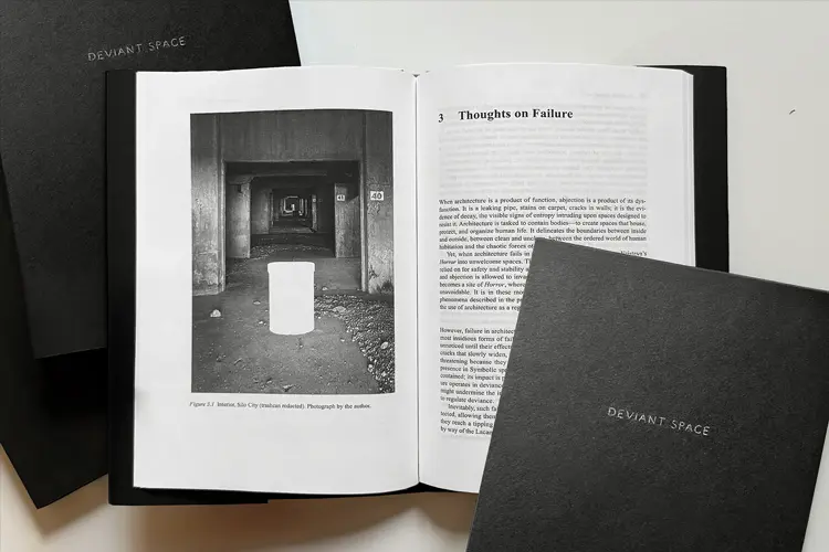 Open book displaying a black-and-white architectural photograph and essay titled “Thoughts on Failure,” with two black covers labeled “Deviant Space.” Open book displaying a black-and-white architectural photograph and essay titled “Thoughts on Failure,” with two black covers labeled “Deviant Space.”