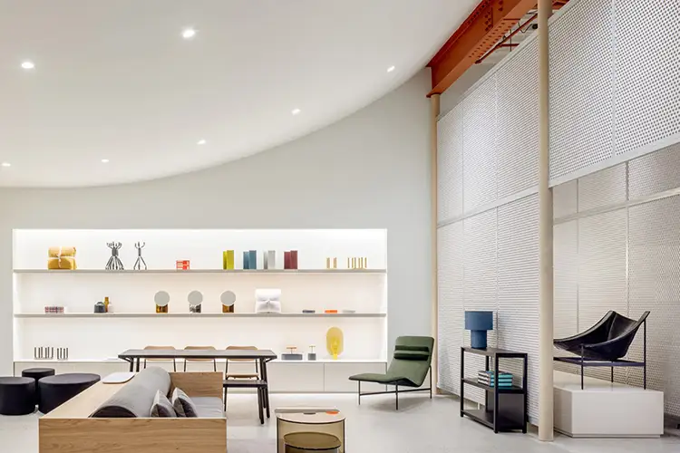 Modern showroom with minimalist furniture, shelving, and perforated partition walls.