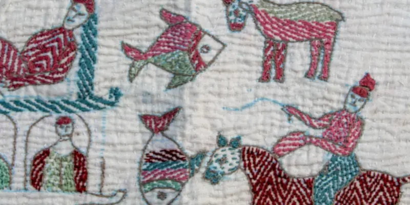 Hand-embroidered textile showing people, animals, and decorative motifs in red, green, and blue thread