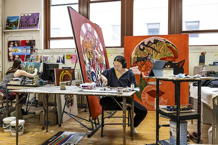 Two artists painting large colorful canvases in a bright studio with wooden floors and windows
