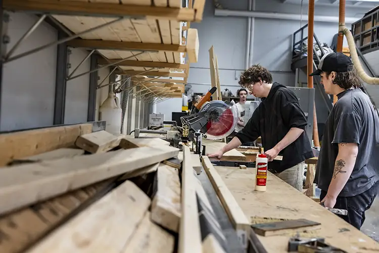 People use a miter saw and woodworking tools in a fabrication workshop.