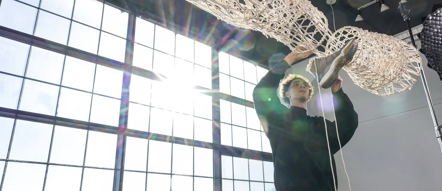 A student works with a suspended sculptural work of art with bright light coming through industrial windows.