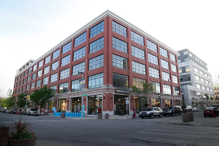 Multi-story red brick building with large industrial windows on a city street corner.