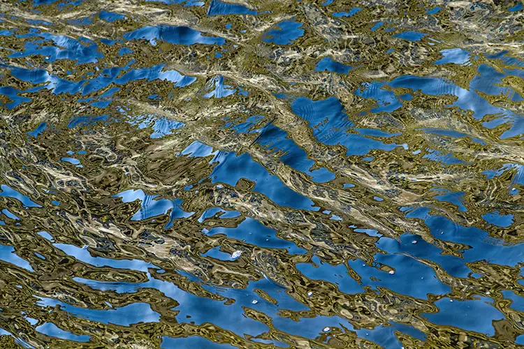 Abstract pattern of rippling water with swirling reflections in blue, green, and gold tones.