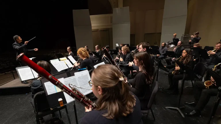 Director Thomas Gamboa stands at the podium with a baton in hand while directing the UWM Wind Ensemble.