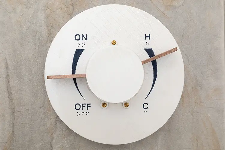Andrew McConville RECENT WORK Custom designed white circular control with ON/OFF and hot/cold settings, mounted on a wall.